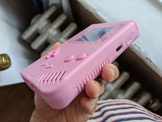 a person holding a pink gameboy phone in their left hand and looking at the camera