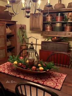 a wooden table topped with a bowl filled with fruit and veggies next to a chandelier