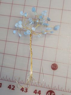 a small tree with blue flowers on top of a piece of paper next to a ruler