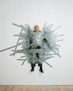 a man standing in front of a white wall with an abstract sculpture on it's side