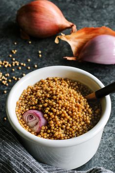 a white bowl filled with lentils next to two onions and an onion on a gray surface