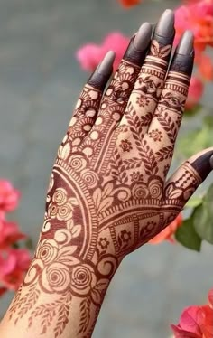 a woman's hand with henna on it and pink flowers in the background