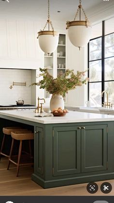 a kitchen with green cabinets and an island in front of a window that has three hanging lights above it