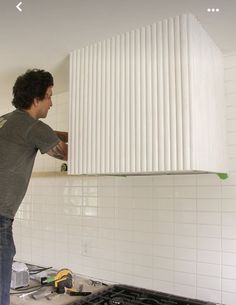 a man standing in front of a stove top oven with white tiles on the wall