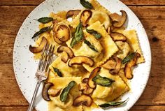 a white plate topped with ravioli covered in mushrooms and sage leaves next to a fork