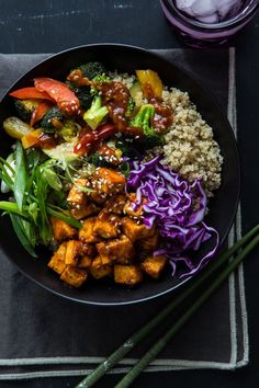 a black plate topped with meat and veggies next to chopsticks on a table