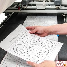 someone is cutting out a pattern on a large sheet of paper with the machine behind them