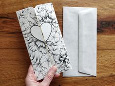 a hand holding an open book with flowers on it next to a white paper box