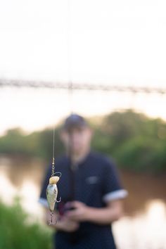 a man standing next to a body of water holding a small fish hanging from it's hook