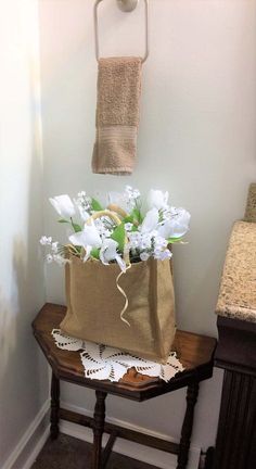 a brown bag with white flowers in it sitting on a small table next to a towel rack