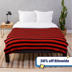 a red and black striped blanket sitting on top of a wooden floor next to a potted plant