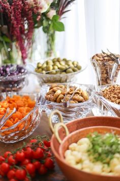 a table topped with bowls filled with different types of food next to vases full of flowers