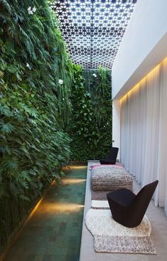 an indoor living area with plants on the walls and flooring, along with two black chairs