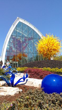 an outdoor garden with blue glass sculptures and yellow flowers in front of a large building