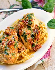 two meatballs covered in sauce and spinach on a white plate with pasta noodles