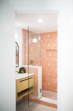 a bathroom with an orange and white tile pattern on the shower wall, vanity sink and mirror