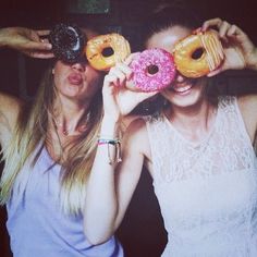 two young women holding up doughnuts to their eyes while standing next to each other