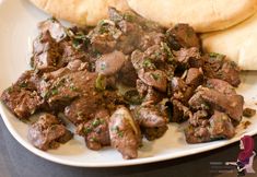 a white plate topped with meat and pita bread next to a baguette