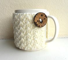 a white coffee cup with a wooden button on the side and a knitted mug sleeve