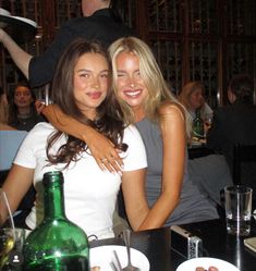 two beautiful young women sitting next to each other in front of a table with food and drinks