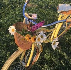 a yellow bicycle with flowers in the basket is parked on some grass and it's sunny