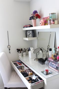 a white desk topped with lots of makeup and other items next to a chair in front of a window