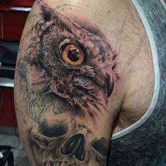 an owl and skull tattoo on the left arm, with orange eyes in it's center