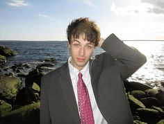 a man in a suit and tie standing by the ocean with headphones on his ears