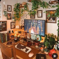 a computer desk with many plants and pictures on the wall