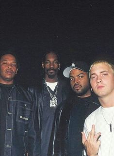 a group of men standing next to each other in front of a dark background with one pointing at the camera