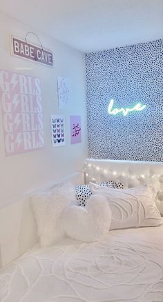 a white bed topped with pillows next to a night stand and neon sign on the wall