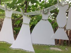 three paper dresses hanging from a clothes line in front of a tree with green leaves