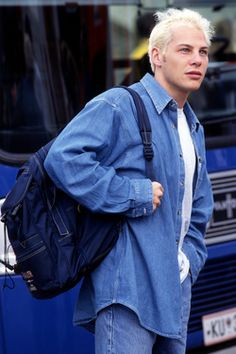 a man with white hair is walking down the street in front of a blue bus