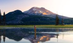 a person standing on a paddle board in front of a lake with mountains in the background