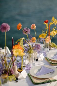 the table is set with plates and vases filled with colorful flowers on top of it