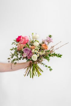 a woman's hand holding a bouquet of flowers on a white background with greenery