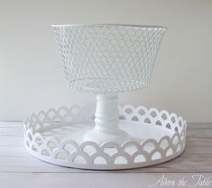 a white cake stand with a wire basket on the top and an empty plate underneath it