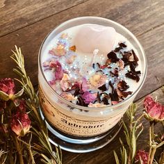 a cup filled with liquid and flowers on top of a wooden table next to plants