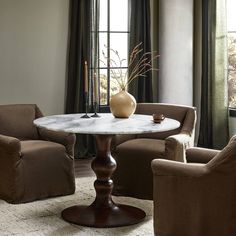 a living room with two chairs, a table and a vase on top of it