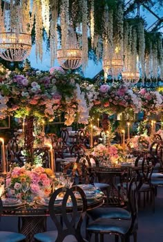 an outdoor dining area with chandeliers hanging from the ceiling and tables covered in flowers