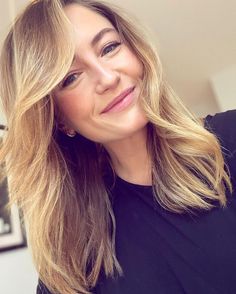 a woman with blonde hair is smiling and looking at the camera while wearing a black shirt