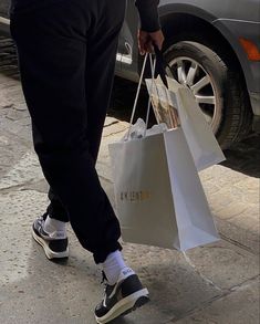 a man is holding shopping bags and walking down the street in front of his car