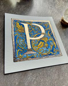 the letter p is painted on top of a piece of blue and yellow paper with gold foil