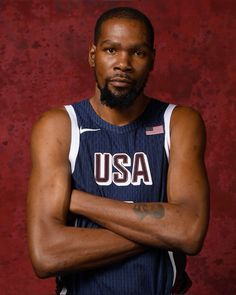 a man with his arms crossed in front of a red background wearing a usa jersey