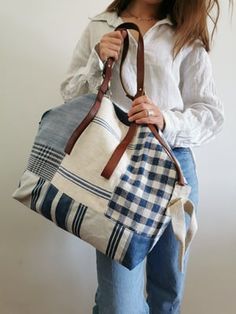 a woman is holding a handbag made out of plaid fabric and leather straps, while standing against a white wall