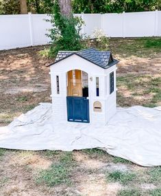 a small white house with a blue door on top of a blanket in the yard