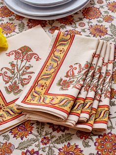 napkins with yellow flowers on them are sitting on a floral tablecloth next to a plate