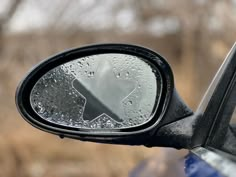 the side view mirror on a car with water droplets all over it and trees in the background