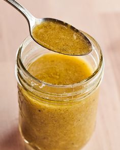 a spoon full of liquid sitting on top of a jar filled with something orange and yellow