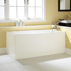 a white bath tub sitting next to a window in a yellow bathroom with tile flooring